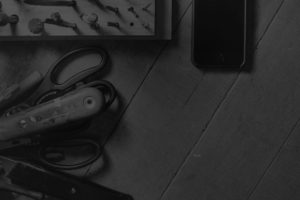Close up black and white image of black iphone sitting on wooden work bench amongst old hand tools